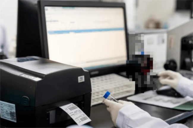 A person operating a pisač barkoda connected to a computer in a clean workspace.